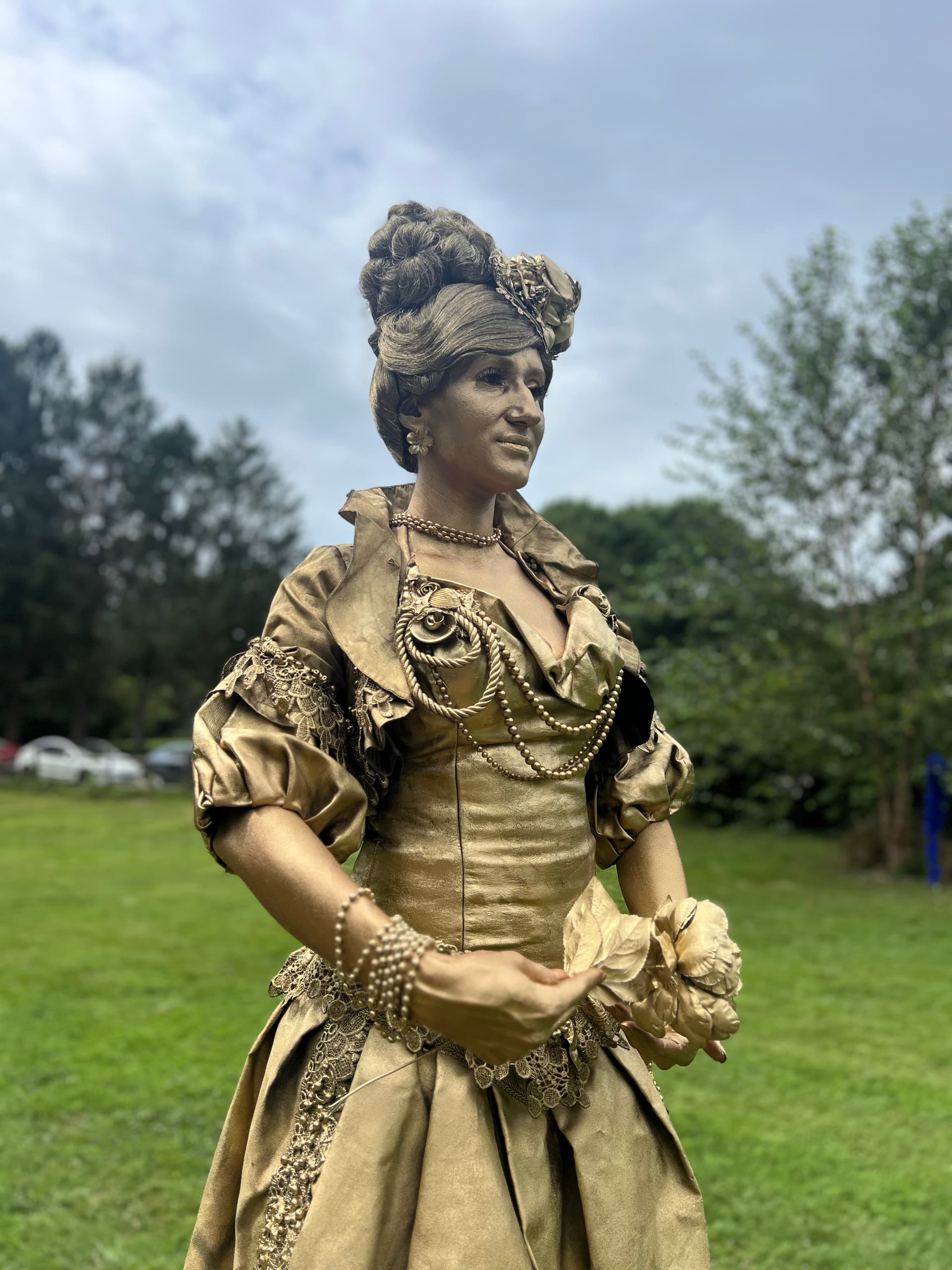 Gold-painted living statue performer posed as a regal queen outdoors